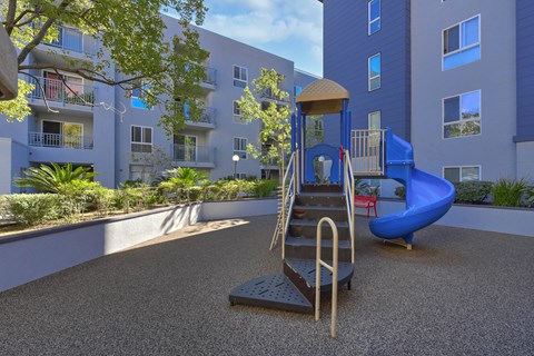 A playground with a slide and a climbing frame in front of a building.