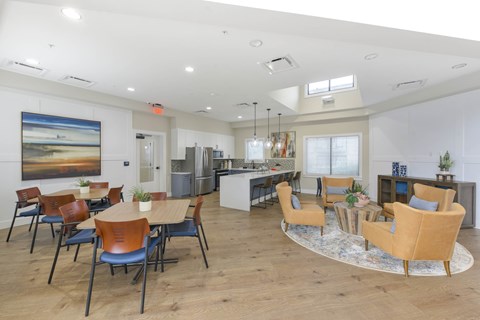 A spacious room with a dining table and chairs, a kitchen area, and a large painting on the wall.