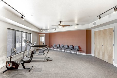 A gym with treadmills, exercise bikes, and a row of chairs.