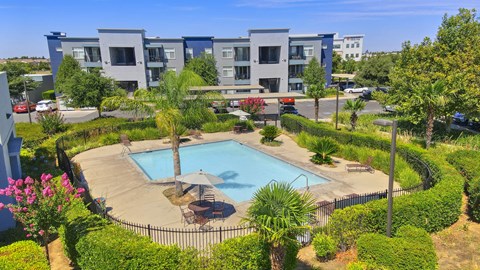 A swimming pool surrounded by a fence and palm trees in front of a building.