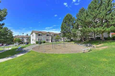 A playground with a swing set and a sandbox in the middle of a grassy area.