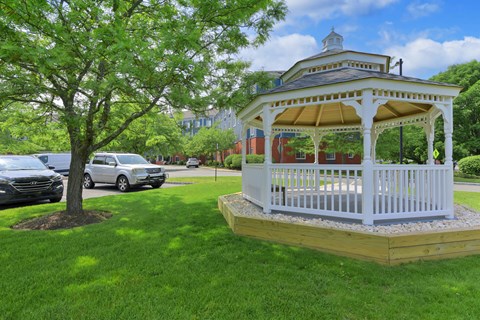 A white gazebo with a yellow roof is surrounded by a grassy area and a tree.