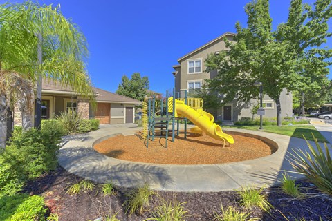 Playground with yellow slide and wood chip safety surface at Whitney Ranch Apartments, California, 95765