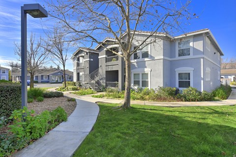 Apartment buildings with curved walkway and landscaping at Corsair Park Senior Apartments, North Highlands, CA 95660