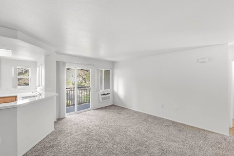 A spacious living room with a carpeted floor and sliding glass doors leading to a balcony.