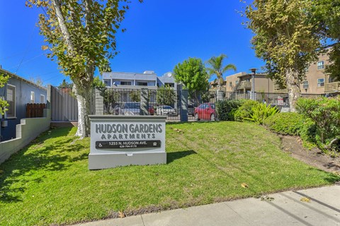 Property entrance monument sign with green lawn and trees at Hudson Gardens Apartments, California, 91104