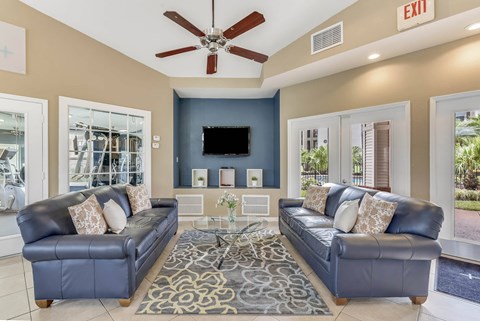A living room with a black leather couch and a ceiling fan.
