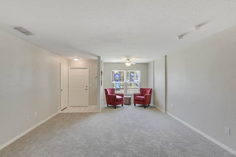 A living room with a grey carpet and two red chairs.