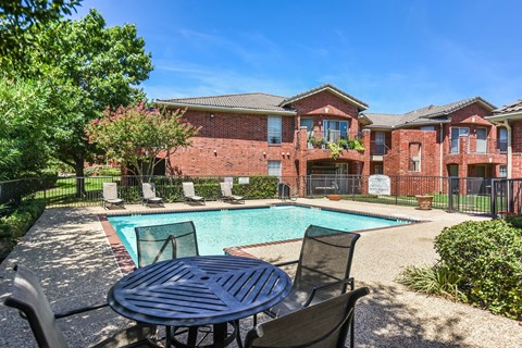 A pool surrounded by a table and chairs in front of a brick building.