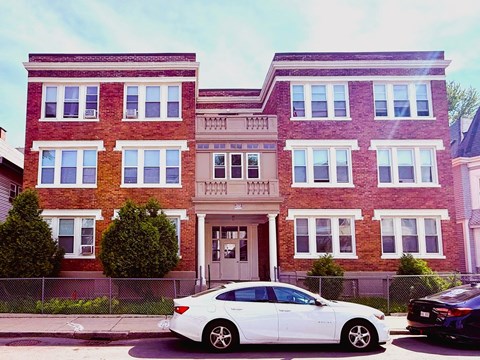 A white car is parked in front of a red brick building.