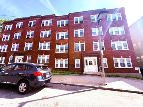 A blue car is parked in front of a red brick building.