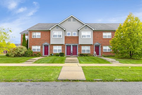 A large brick house with a red door and a green lawn in front.