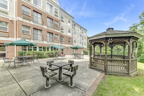 A gazebo is situated in a courtyard with a picnic table and chairs.