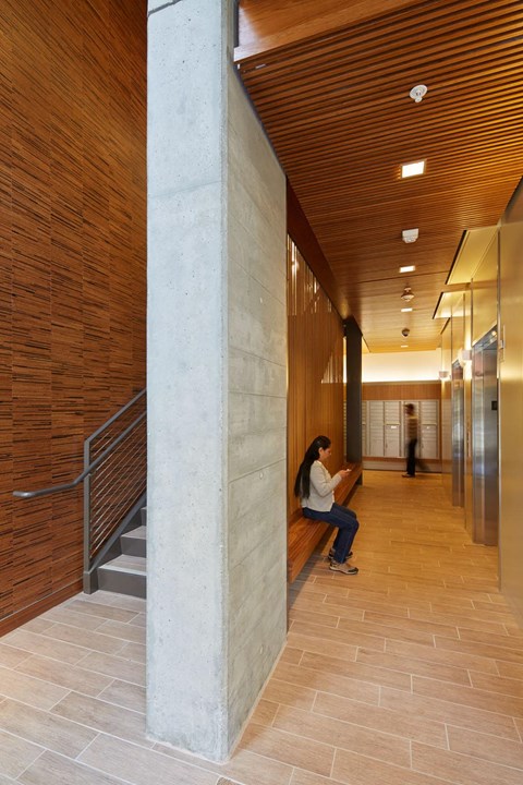 A woman sits on a bench in a hallway with a wooden ceiling.