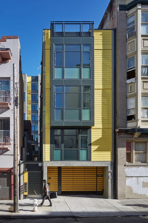 A man walking a dog in front of a yellow building.