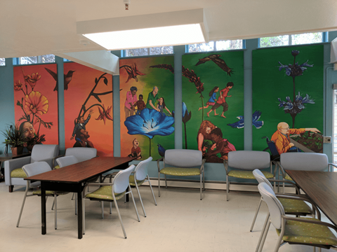 A room with a long table and chairs with a mural on the wall.