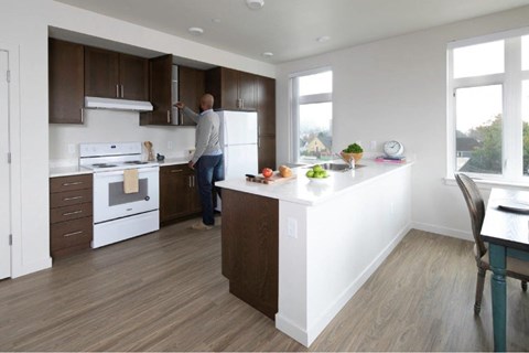 A man is standing in a kitchen with a white counter and brown cabinets.