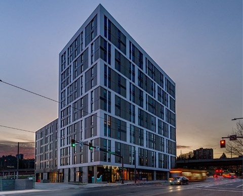 A tall building with many windows is lit up at dusk.