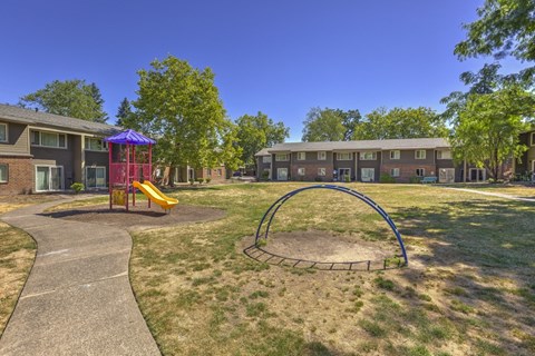 A playground with a slide and a roundabout in front of apartment buildings.
