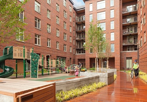 A playground area with a green slide and a person riding a bicycle.
