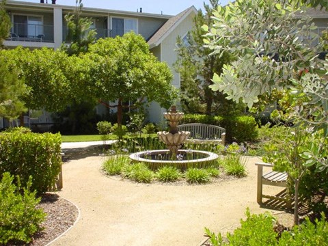 A garden with a fountain and bench in front of a building.