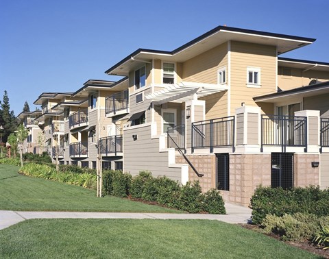 A row of townhouses with balconies and a green lawn in front.