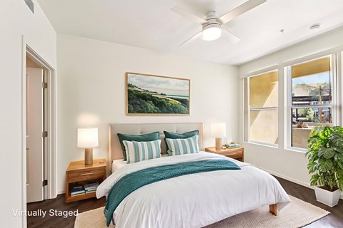 A bedroom with a bed, pillows, a ceiling fan, and a painting on the wall.