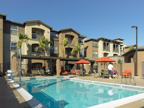 A swimming pool in front of apartment buildings with people relaxing.