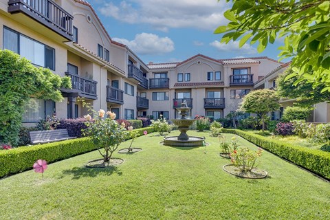 A courtyard with a fountain and flower beds in front of apartment buildings.