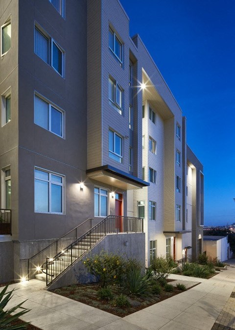 A modern apartment building with a well-lit entrance and landscaping.