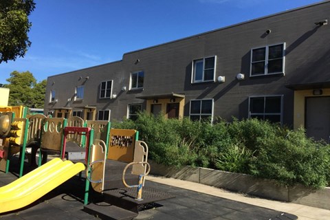 A playground with a yellow slide in front of a grey building.