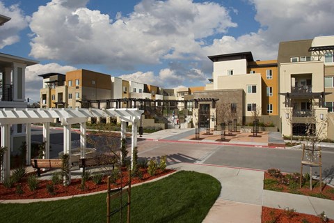A view of a courtyard with a white pergola and a bench.