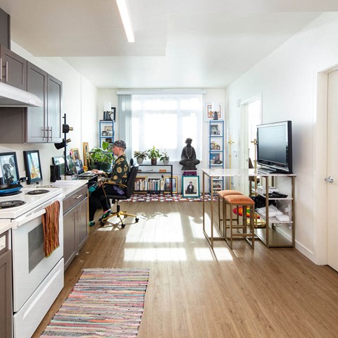 A person is sitting on a chair in a room with a kitchen area to the left.