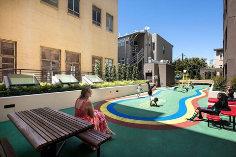 A woman in a pink dress sits on a bench in a colorful playground.