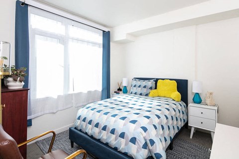 A bedroom with a bed, nightstand, chair, and window.