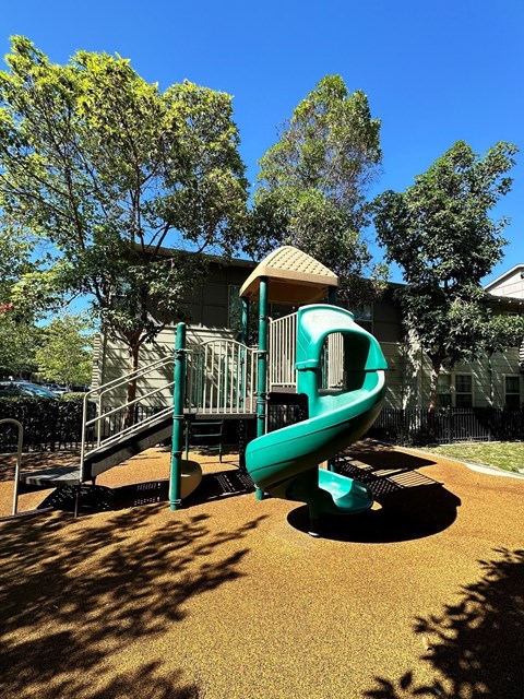 A playground with a green slide and a brown sandbox.