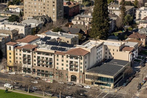 A large building with a red roof is surrounded by other buildings.