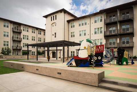 A playground area with a slide and a teddy bear slide in front of a building.