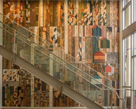A staircase with a glass railing and a mosaic wall on the side.