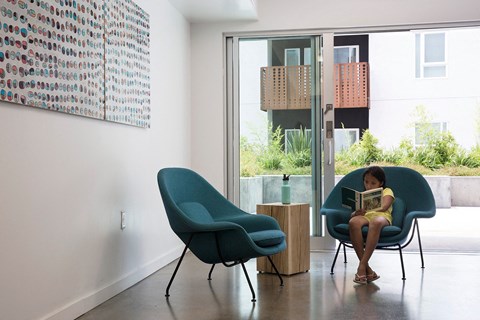 A woman is sitting on a blue chair reading a book.