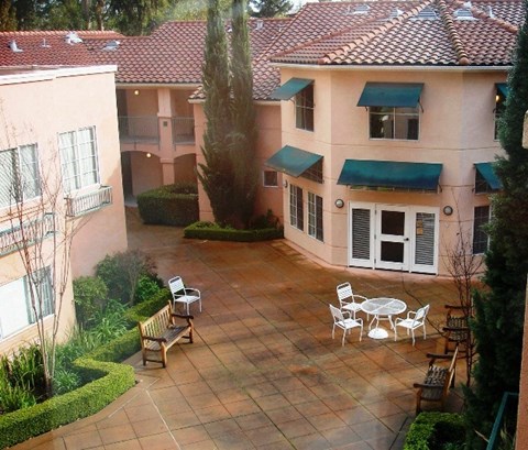 A patio with a table and chairs is surrounded by bushes and trees.