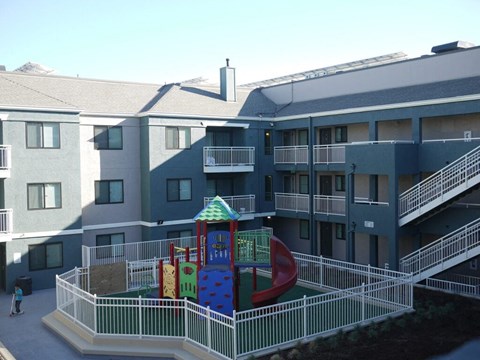 A playground with a slide and a climbing frame in front of a building.