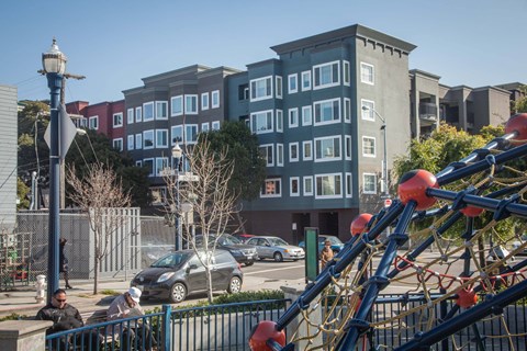 A playground with a blue fence and a slide in front of a building.