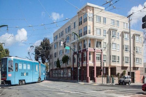 A blue tram is on a street in front of a building.