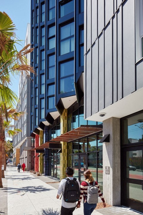 Two people walking down a sidewalk past a building with a glass facade.