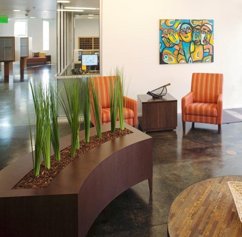 A modern office lobby with orange chairs and a wooden planter.