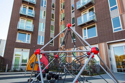 A playground structure with red and yellow elements in front of a brick building.