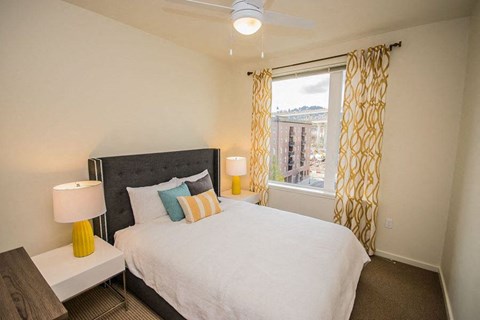 A bedroom with a large bed, a nightstand with a lamp, and a window with curtains.