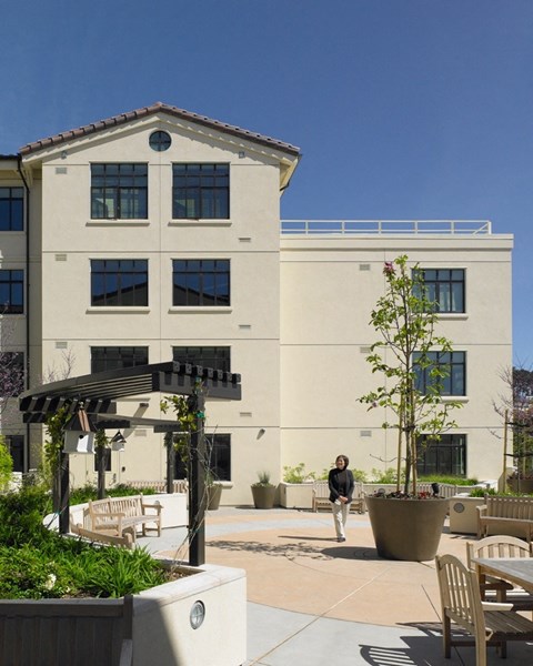 A woman walks past a tree in front of a building.