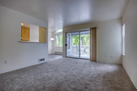 A spacious room with a grey carpet and a sliding glass door leading to a balcony.
